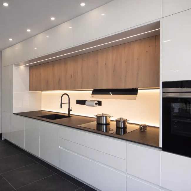 Cucina moderna lineare con ante bianche lucide, pensili in legno naturale, piano nero e illuminazione LED integrata, in promozione showroom a Bolzano.