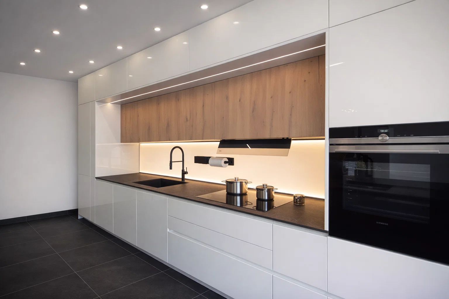 Cucina moderna lineare con ante bianche lucide, pensili in legno naturale, piano nero e illuminazione LED integrata, in promozione showroom a Bolzano.